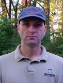 Picture of a clean-shaven man wearing a blue KA-BAR baseball cap with red lettering and a grey polo.